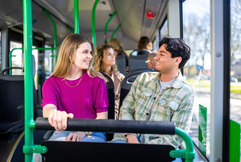 Een jongen in geblokt overhemd en meisje in een roze shirt zitten in een bus en kijken glimlachend naar elkaar